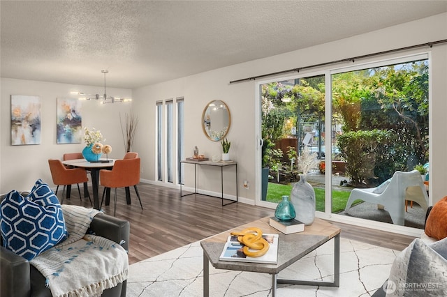 living area with baseboards, a textured ceiling, wood finished floors, and a notable chandelier
