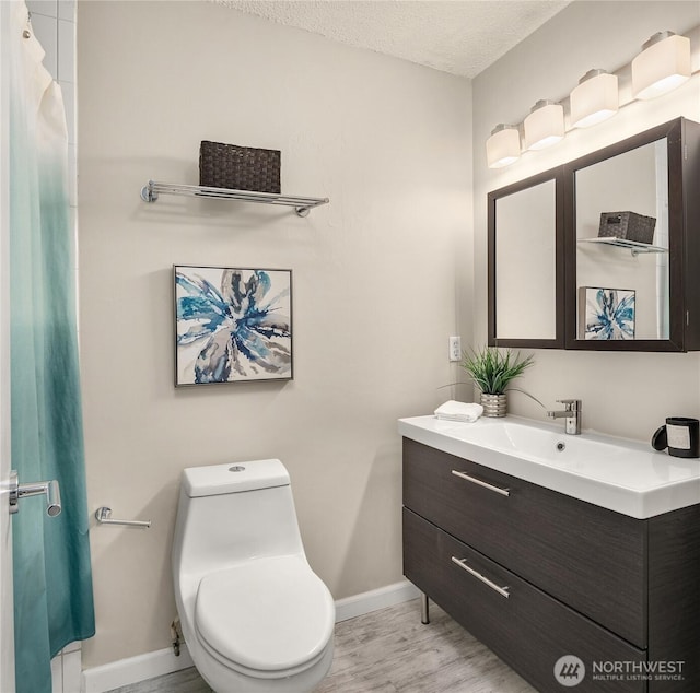 full bathroom featuring a textured ceiling, wood finished floors, baseboards, vanity, and toilet