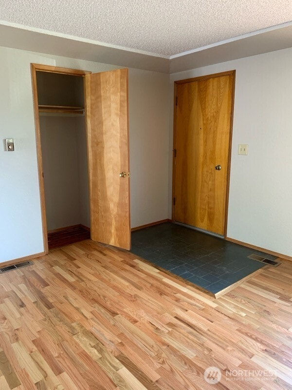 unfurnished bedroom featuring baseboards, a closet, a textured ceiling, and wood finished floors