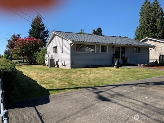 view of front of house with cooling unit, a front lawn, and metal roof