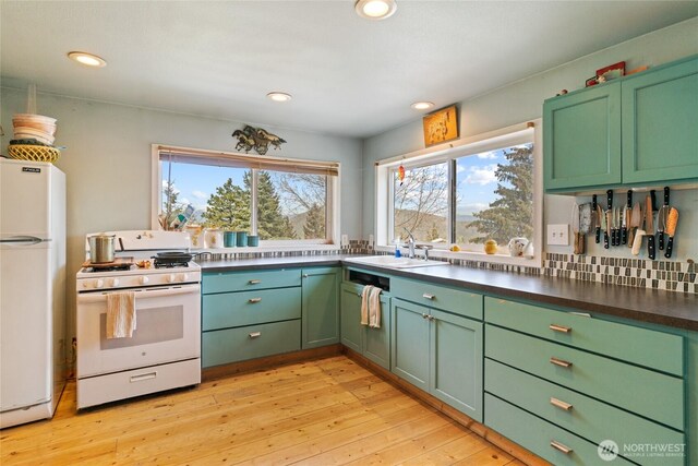 kitchen with dark countertops, white appliances, green cabinetry, a sink, and light wood-style flooring