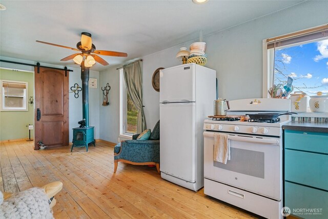 kitchen featuring ceiling fan, dark countertops, a wood stove, white appliances, and light wood-style flooring