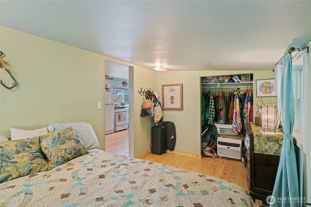 bedroom with freestanding refrigerator, wood-type flooring, and a closet