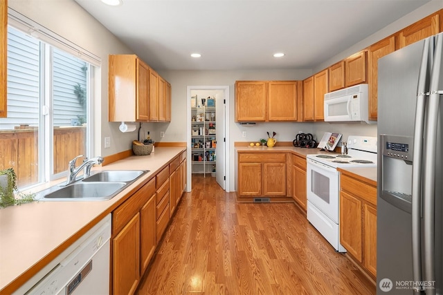 kitchen with light wood-type flooring, a sink, light countertops, recessed lighting, and white appliances