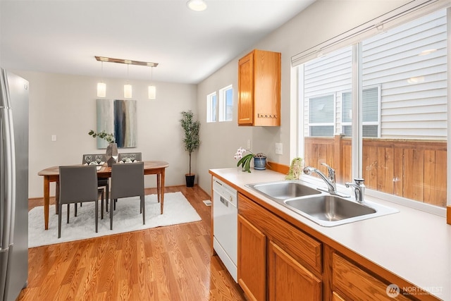 kitchen featuring light wood-type flooring, dishwasher, a sink, light countertops, and freestanding refrigerator
