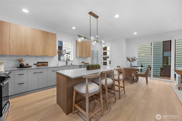kitchen with a sink, light countertops, a kitchen breakfast bar, modern cabinets, and black range with electric stovetop