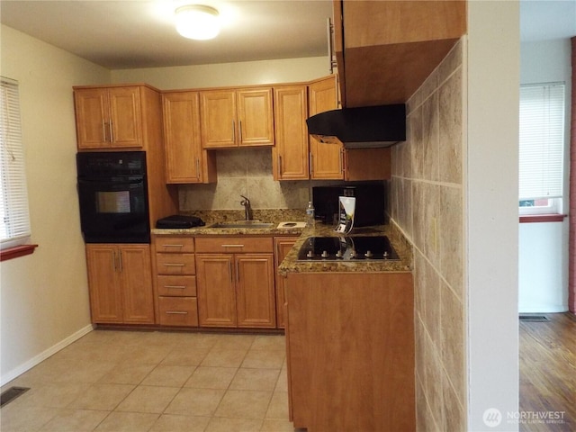 kitchen featuring oven, cooktop, a sink, baseboards, and brown cabinetry