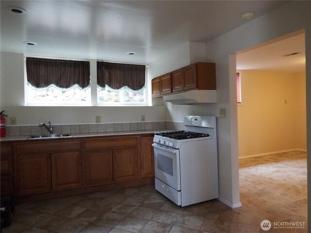 kitchen with white range with gas stovetop, under cabinet range hood, a sink, and light countertops