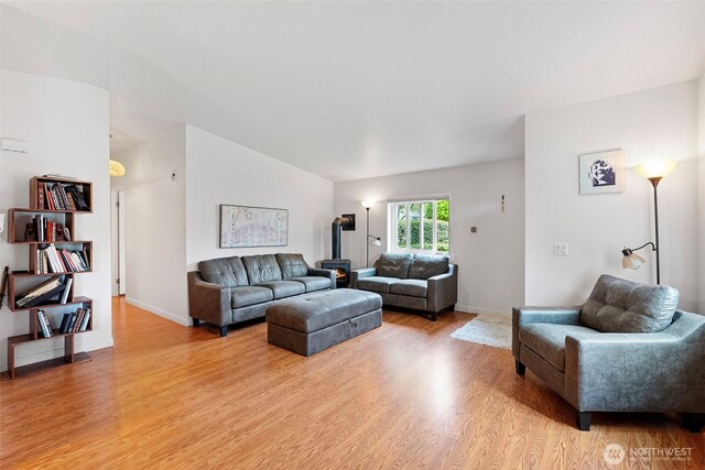 living area with a wood stove, baseboards, light wood-style flooring, and lofted ceiling