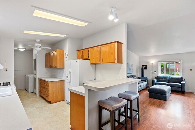 kitchen featuring a peninsula, washer / clothes dryer, a kitchen breakfast bar, white refrigerator with ice dispenser, and light countertops