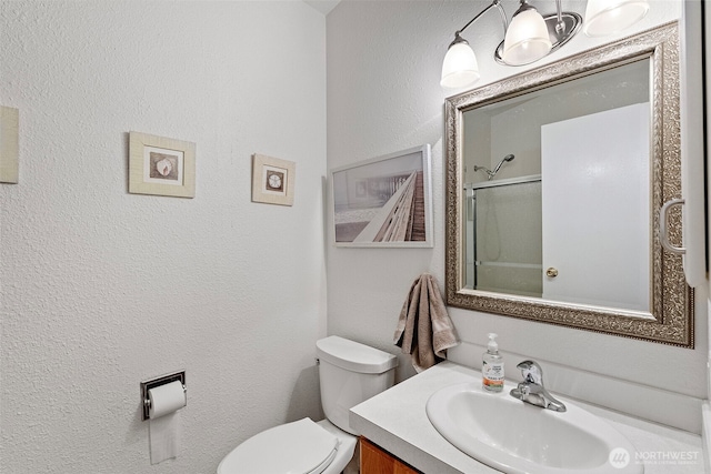 bathroom featuring toilet, a shower with door, a textured wall, and vanity