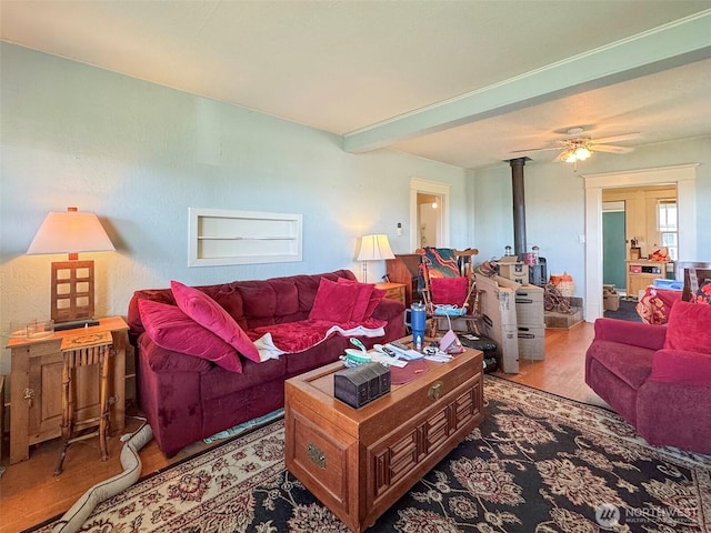 living area with wood finished floors, a wood stove, ceiling fan, and beam ceiling