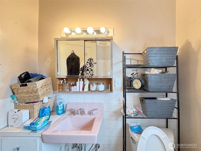 half bath featuring toilet, a sink, tasteful backsplash, and a textured wall