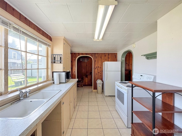 kitchen featuring white appliances, a sink, arched walkways, wood walls, and light countertops
