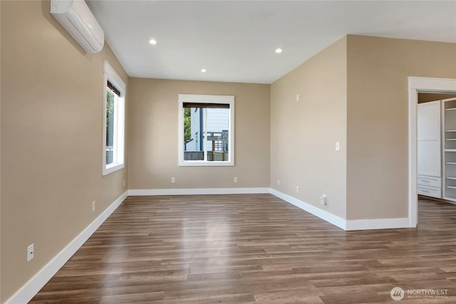 empty room with baseboards, a wall mounted AC, and wood finished floors