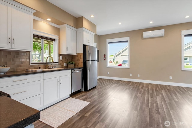 kitchen with dark countertops, appliances with stainless steel finishes, a sink, an AC wall unit, and wood finished floors