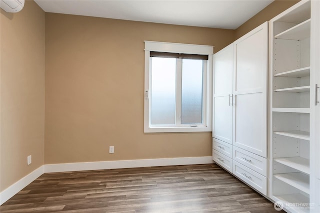 unfurnished bedroom featuring dark wood-type flooring, baseboards, and a wall unit AC