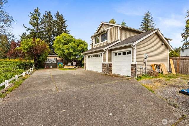 view of side of home featuring roof with shingles, fence, stone siding, and aphalt driveway