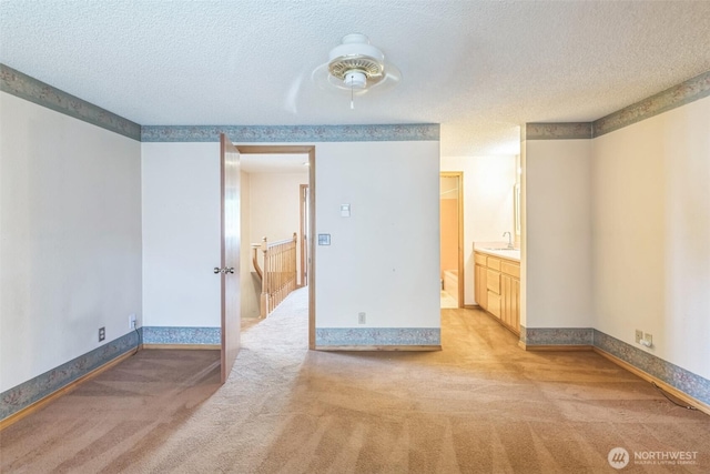 unfurnished room featuring a sink, baseboards, a textured ceiling, and light colored carpet