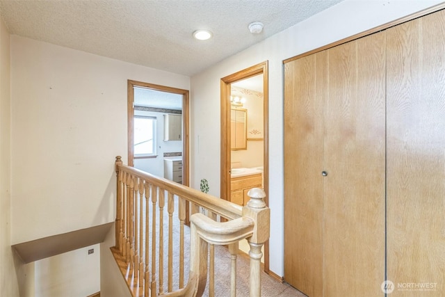 hall featuring carpet floors, a textured ceiling, and an upstairs landing