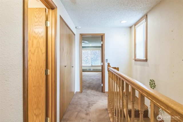 hallway with a textured ceiling, visible vents, an upstairs landing, a textured wall, and light carpet