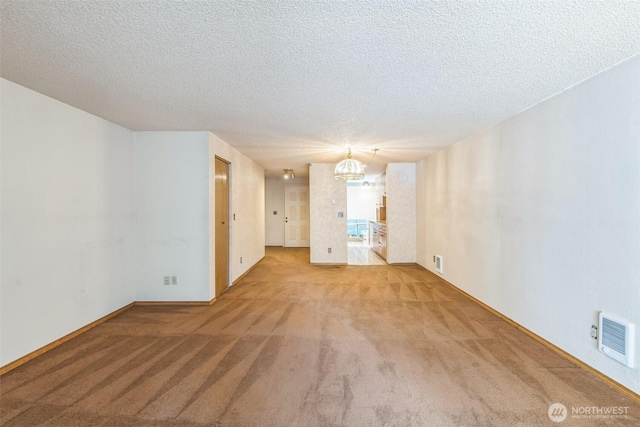 empty room featuring an inviting chandelier, carpet flooring, a textured ceiling, and visible vents