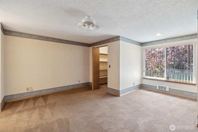 carpeted spare room with ceiling fan, a textured ceiling, visible vents, and baseboards