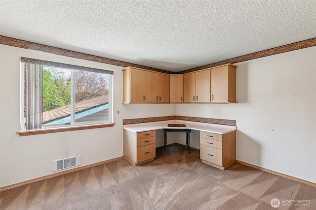 unfurnished office with a textured ceiling, visible vents, light carpet, and built in study area