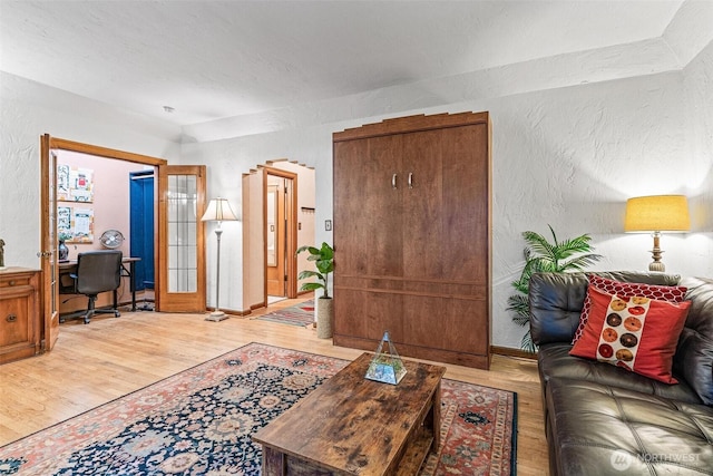 living area featuring light wood-style flooring, a textured wall, a desk, and baseboards