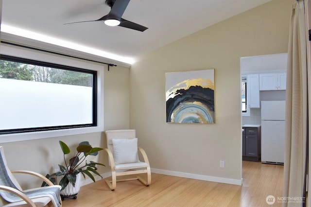 living area featuring light wood-style floors, baseboards, ceiling fan, and vaulted ceiling