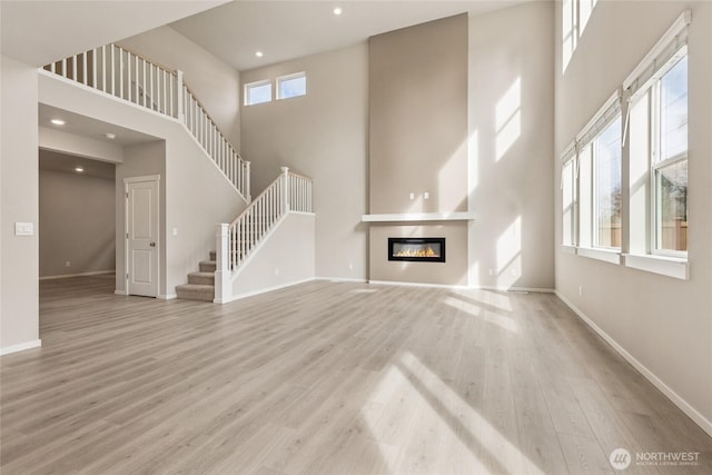 unfurnished living room featuring baseboards, a glass covered fireplace, a towering ceiling, and wood finished floors