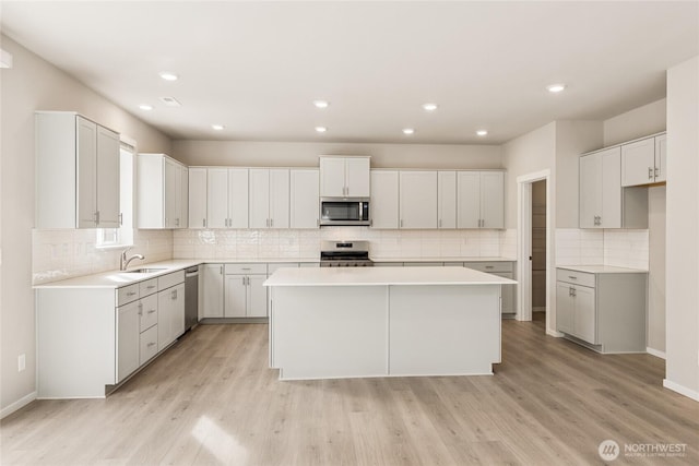 kitchen featuring decorative backsplash, a kitchen island, appliances with stainless steel finishes, a sink, and light wood finished floors