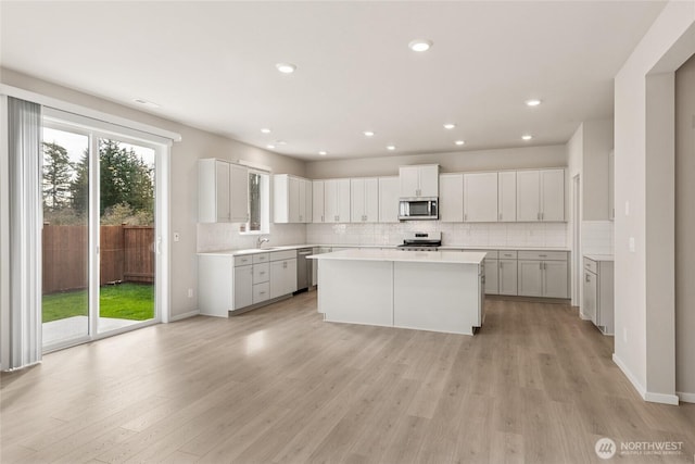 kitchen with decorative backsplash, a center island, light countertops, light wood finished floors, and appliances with stainless steel finishes