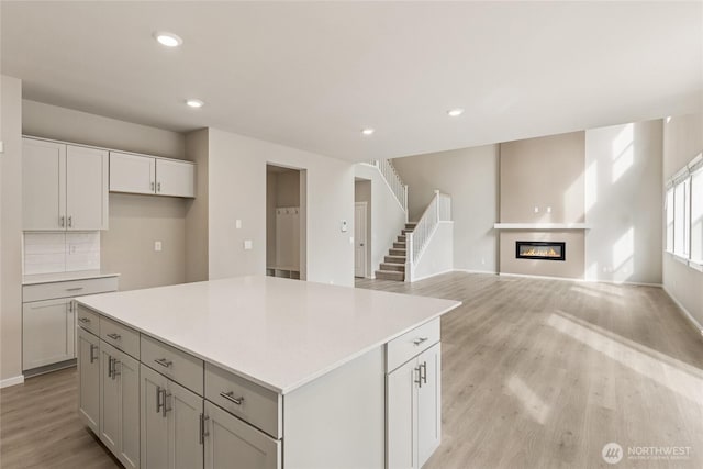 kitchen with a center island, light countertops, a glass covered fireplace, recessed lighting, and light wood-style flooring