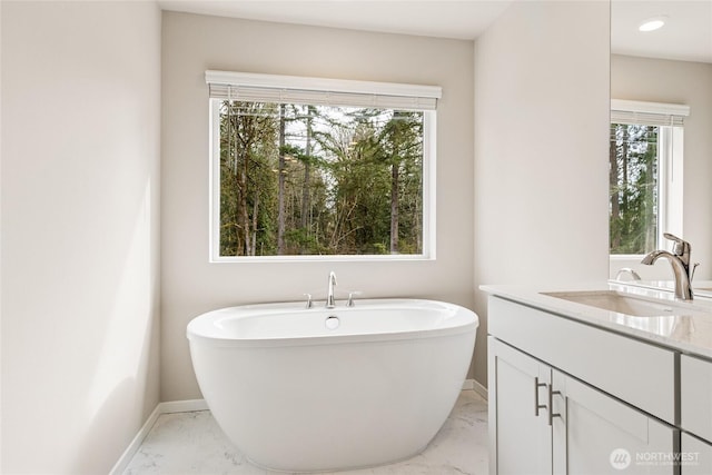 full bathroom featuring baseboards, marble finish floor, a freestanding bath, and vanity
