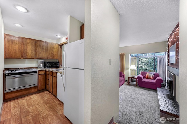 kitchen with brown cabinets, a textured wall, light wood-style floors, white appliances, and open floor plan