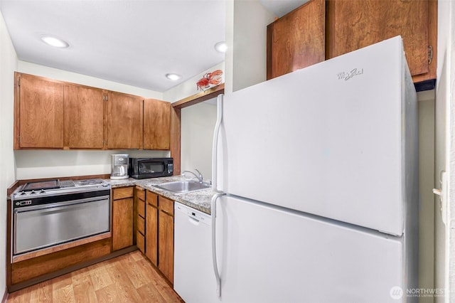 kitchen featuring brown cabinetry, a sink, light wood-style flooring, and white appliances