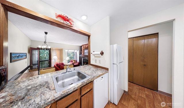 kitchen featuring brown cabinets, a notable chandelier, a sink, white appliances, and baseboards