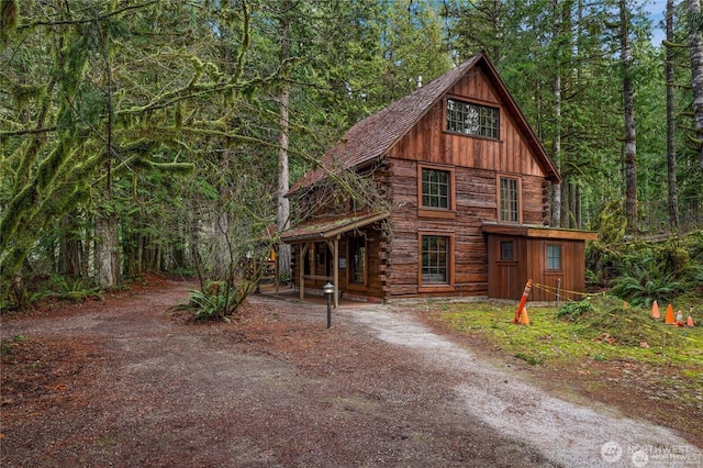 cabin with a porch, a view of trees, and log siding