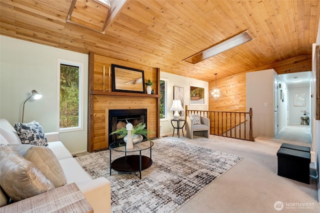 carpeted living area with wooden walls, wood ceiling, vaulted ceiling with skylight, and a large fireplace