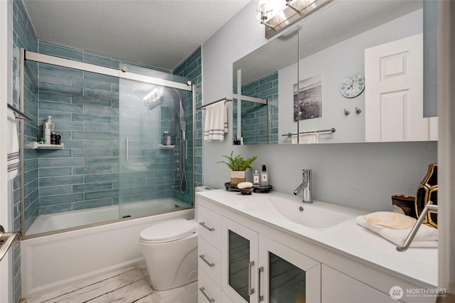 full bath with shower / bath combination with glass door, tile patterned flooring, vanity, toilet, and a textured ceiling
