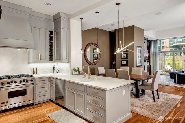 kitchen with a peninsula, custom exhaust hood, a sink, premium range, and gray cabinetry