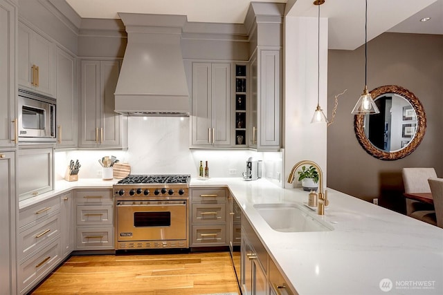 kitchen featuring decorative light fixtures, appliances with stainless steel finishes, a sink, custom exhaust hood, and light wood-style floors
