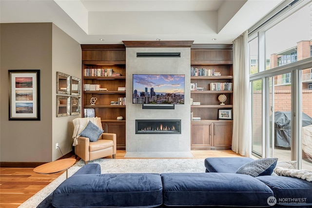 living room featuring baseboards, built in features, wood finished floors, and a tile fireplace