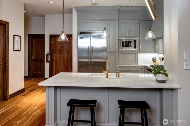 kitchen with light wood-type flooring, a sink, gray cabinetry, a peninsula, and built in appliances