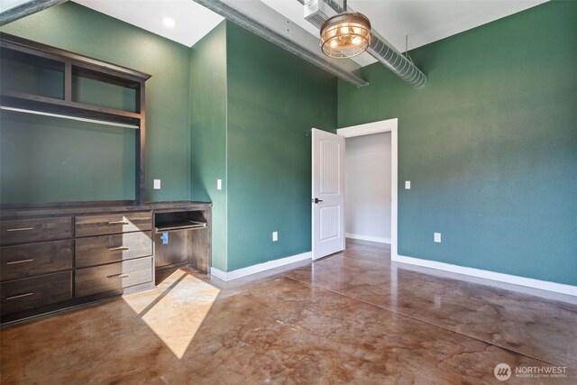 unfurnished bedroom with concrete flooring, a high ceiling, and baseboards