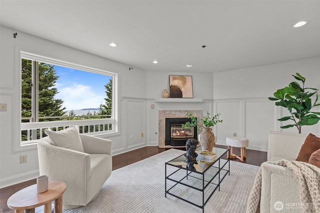 living room featuring a tiled fireplace, a decorative wall, recessed lighting, and wood finished floors