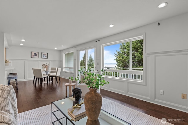 living room featuring recessed lighting, dark wood-style flooring, a decorative wall, and a wainscoted wall