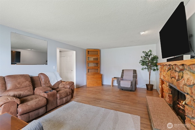 living area with light wood-type flooring, a stone fireplace, and a textured ceiling