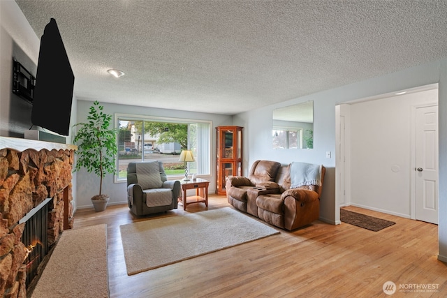 living area featuring a textured ceiling, baseboards, a stone fireplace, and light wood-style floors